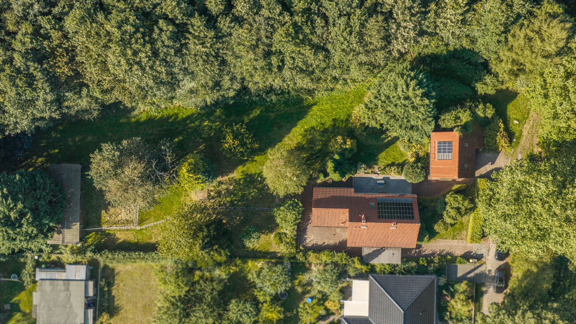 Luftaufnahme eines Hauses mit rotem Dach und Garten, umgeben von viel Grün.