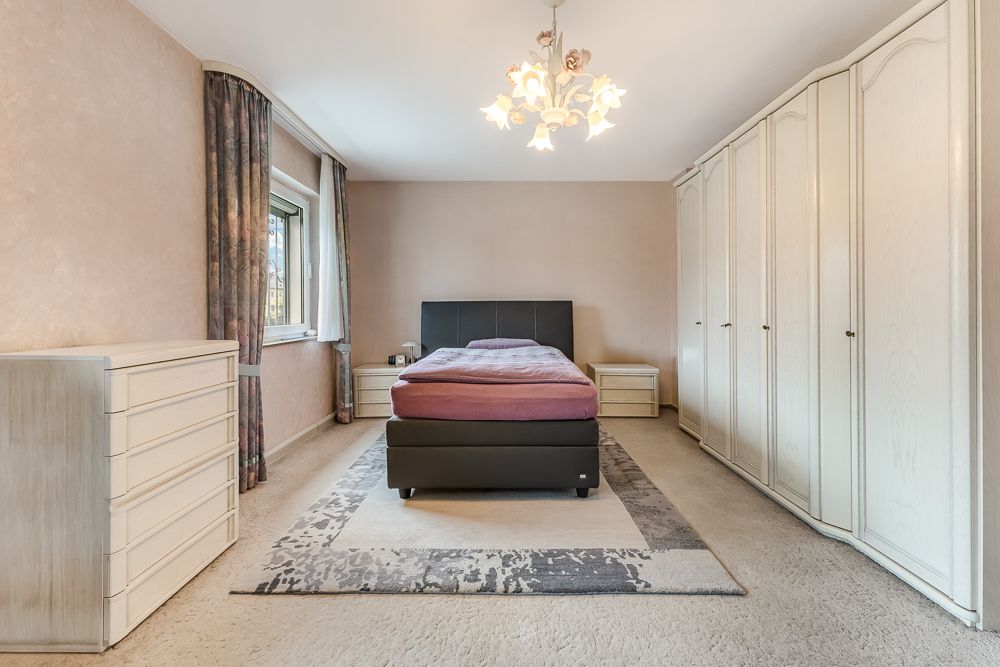 Schlafzimmer mit Doppelbett, großem Kleiderschrank, Kommode und Fenster mit Vorhängen.