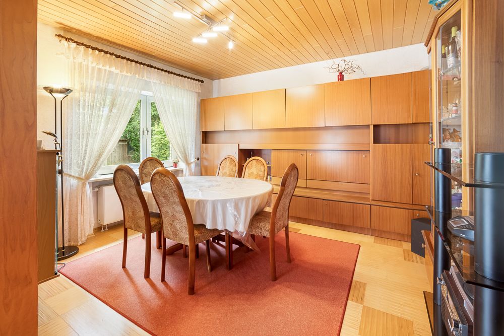 Esszimmer mit rundem Tisch, sechs Stühlen, Holzdecke und großen Holzschränken an der Wand.