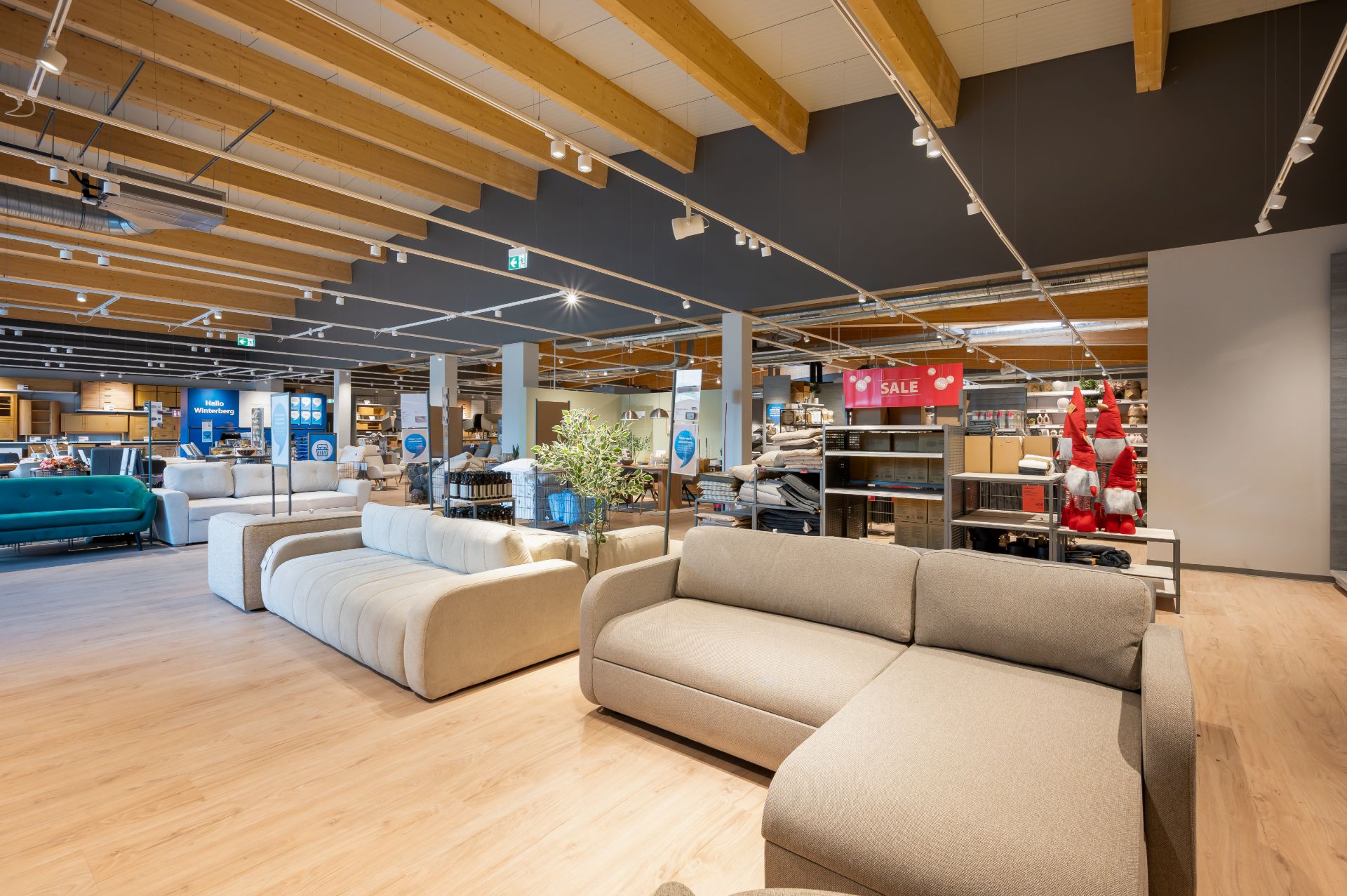 Großer Raum mit modernen Sofas, Holzboden und sichtbaren Deckenbalken, daneben Dekorationsartikel.