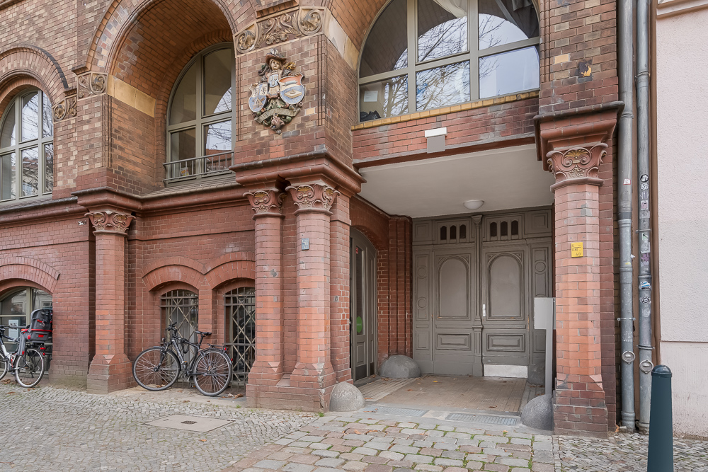 Eingang eines Altbauwohnhauses mit Ziegelsteinfassade und Fahrrädern vor dem Gebäude.