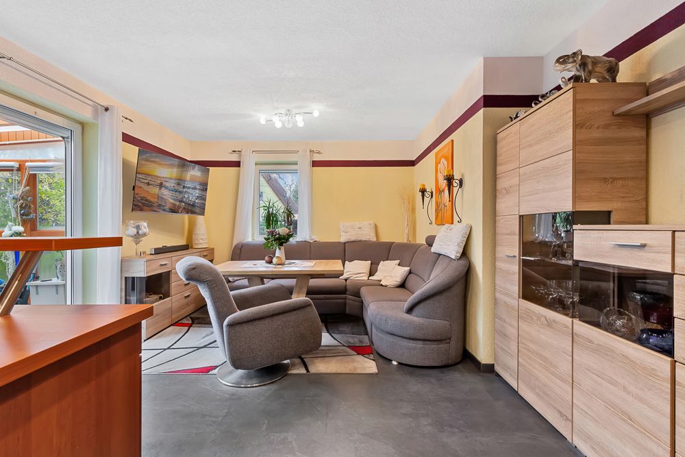 Wohnzimmer mit grauer Eckcouch, Sessel, Holzmöbeln und großem Fenster.