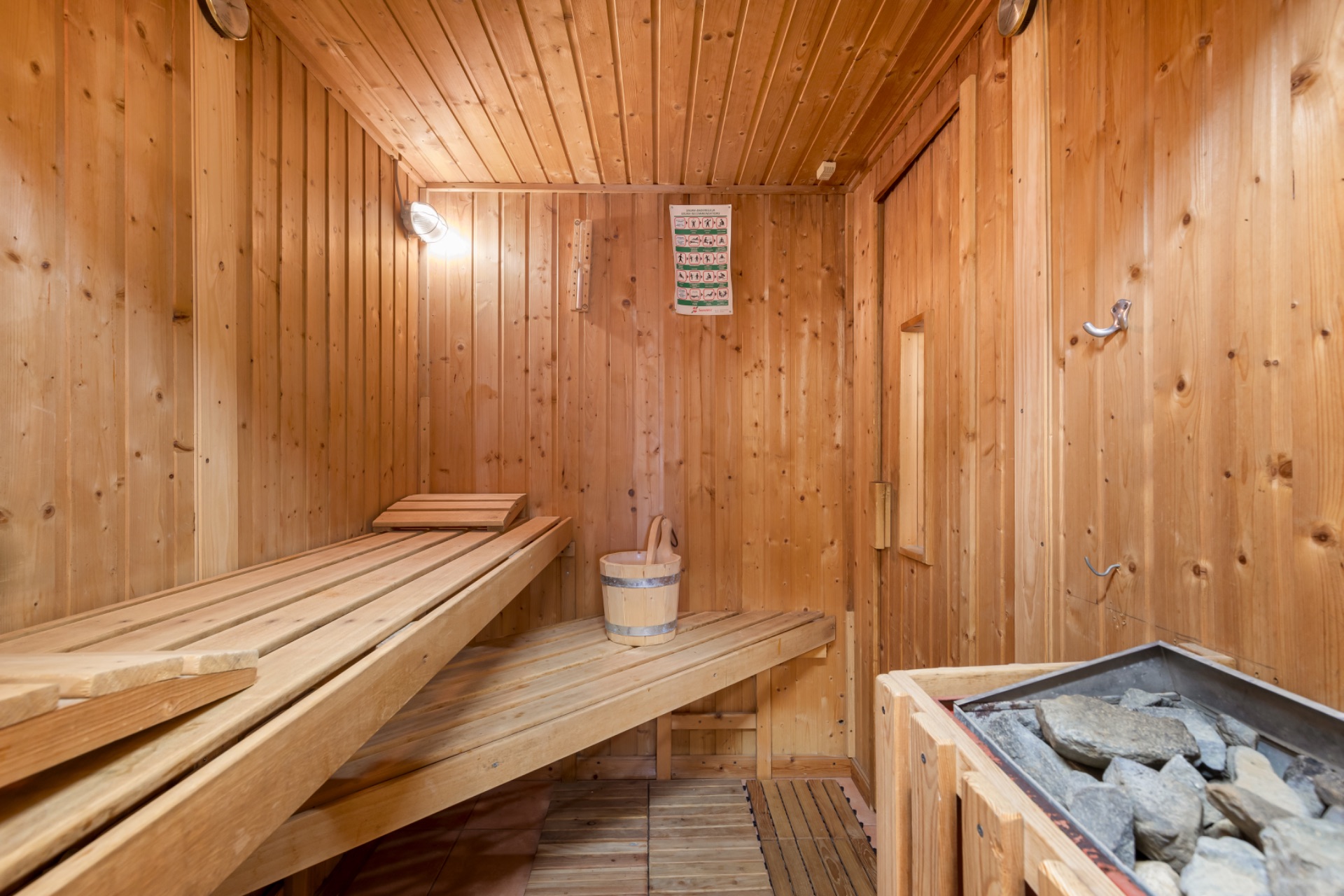 Holzsauna mit Bänken, Saunaofen mit Steinen und Eimer auf unterer Bank.