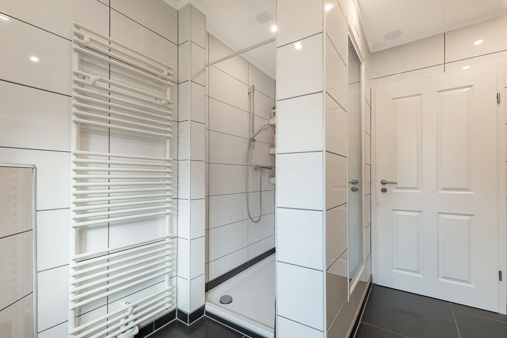 Modernes Badezimmer mit Dusche, weißem Handtuchheizkörper und weißen Fliesen.