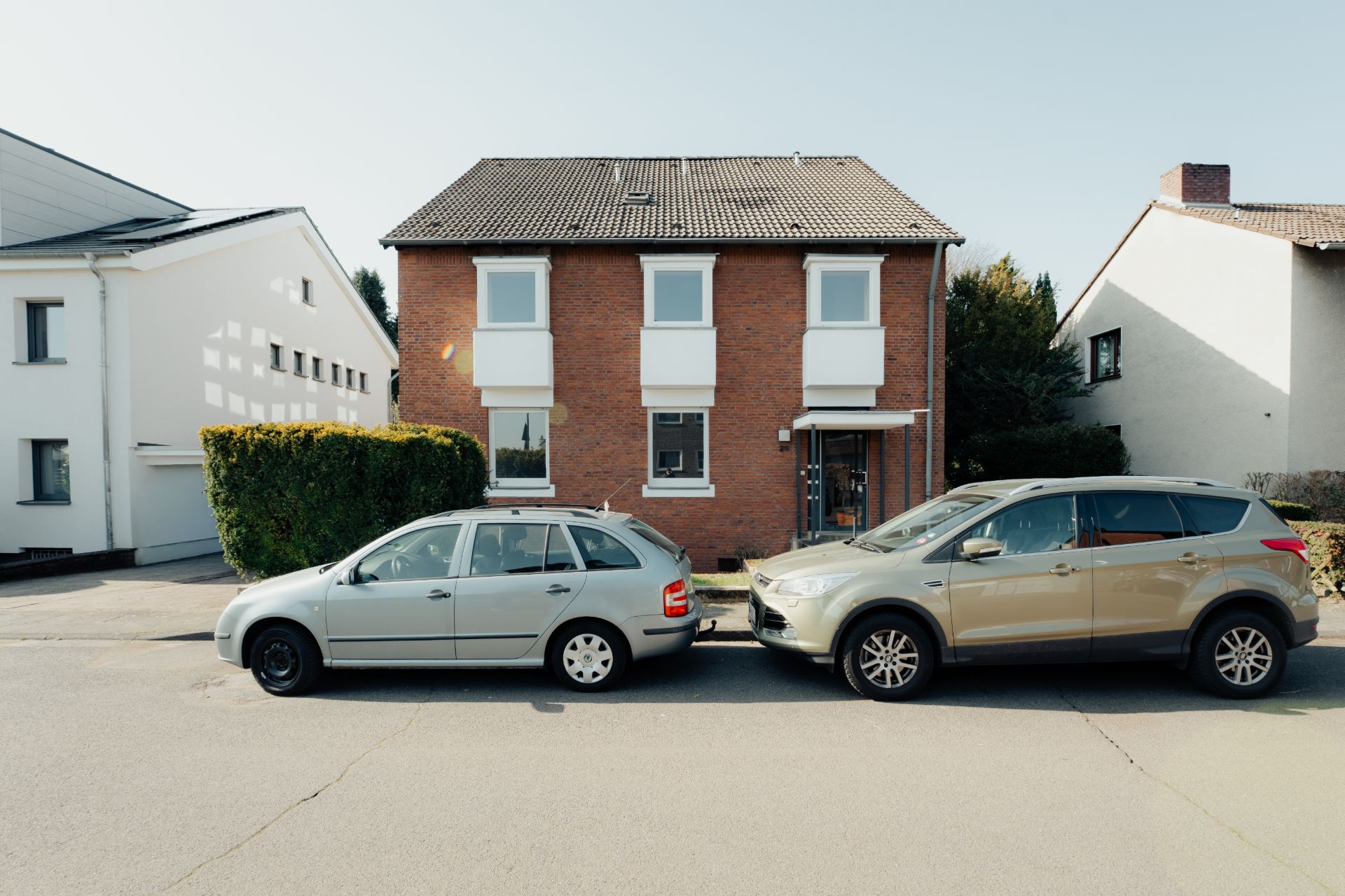 Zwei Autos parken vor einem zweistöckigen Backsteinhaus mit drei Fenstern im Obergeschoss.