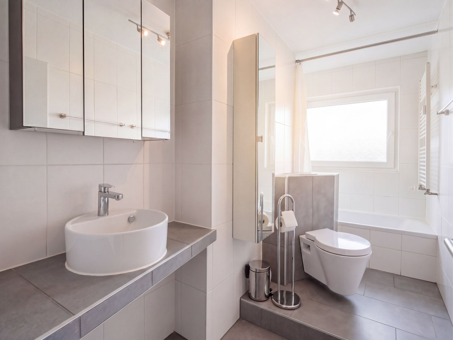 Modernes Badezimmer mit Waschbecken, Wandspiegel, Toilette und Badewanne.