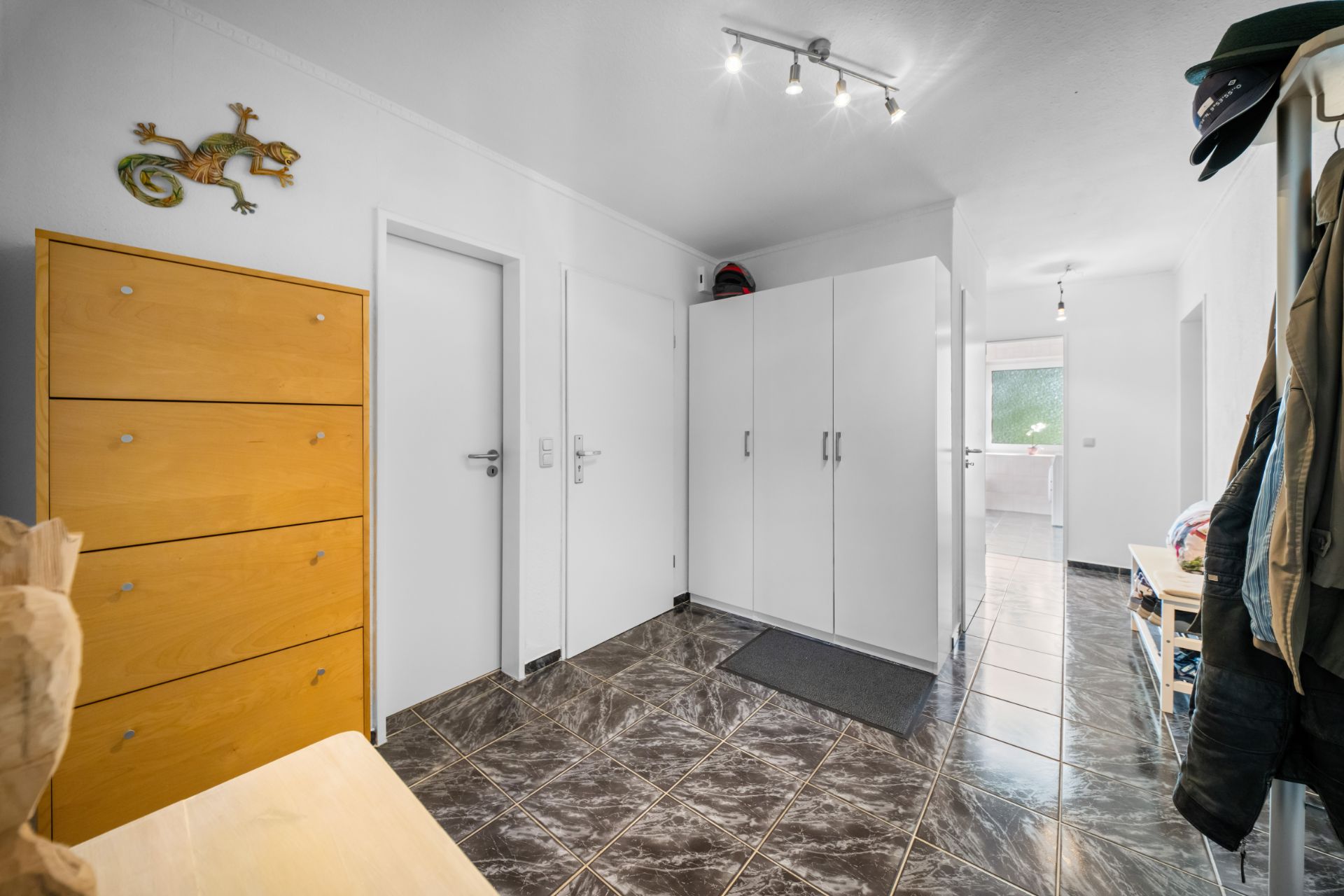 Flur mit Fliesenboden, weißen Schränken, Garderobe und gelbem Schuhschrank.