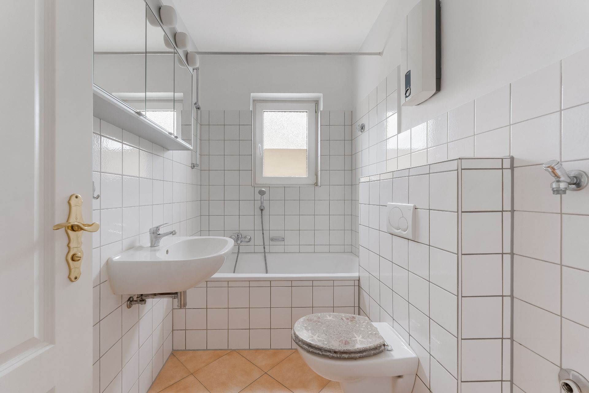 Helles Badezimmer mit Badewanne, Waschbecken, Toilette und Fenster, weiße Fliesen an den Wänden.