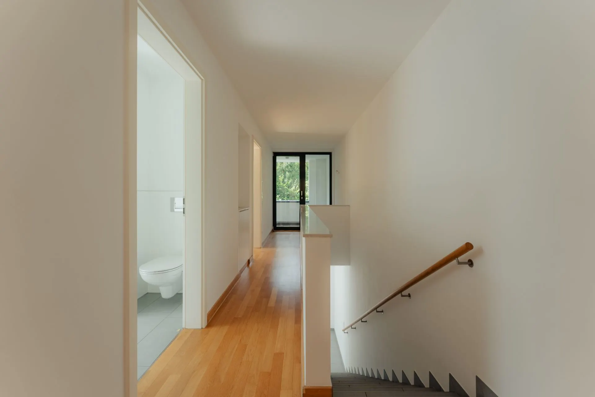 Heller Flur mit Holzfußboden, Treppe, offenem WC und Glastür zum Balkon.