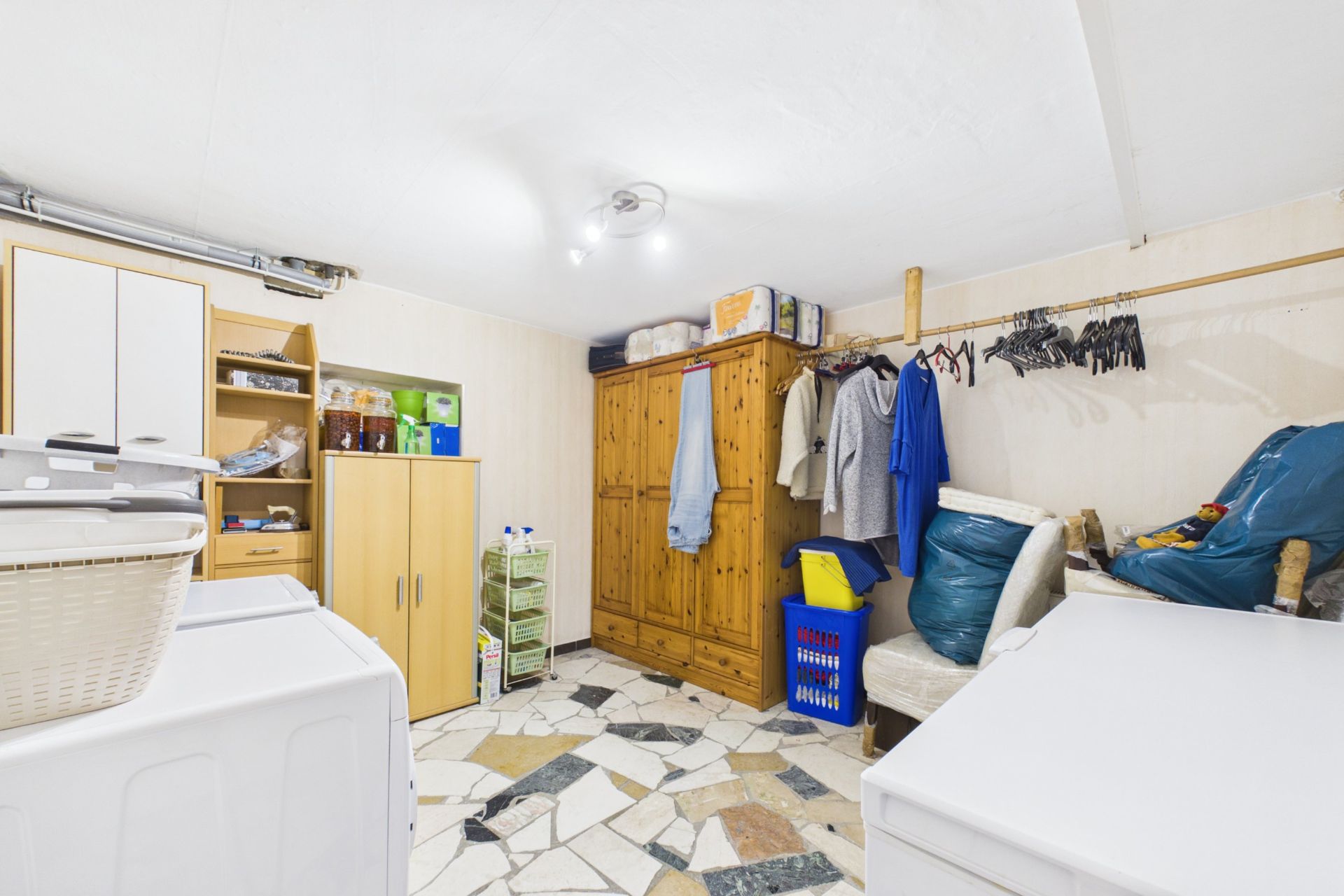 Waschküche mit Schränken, Waschmaschine, Trockner und Wäscheständer in einem Wohnhaus.