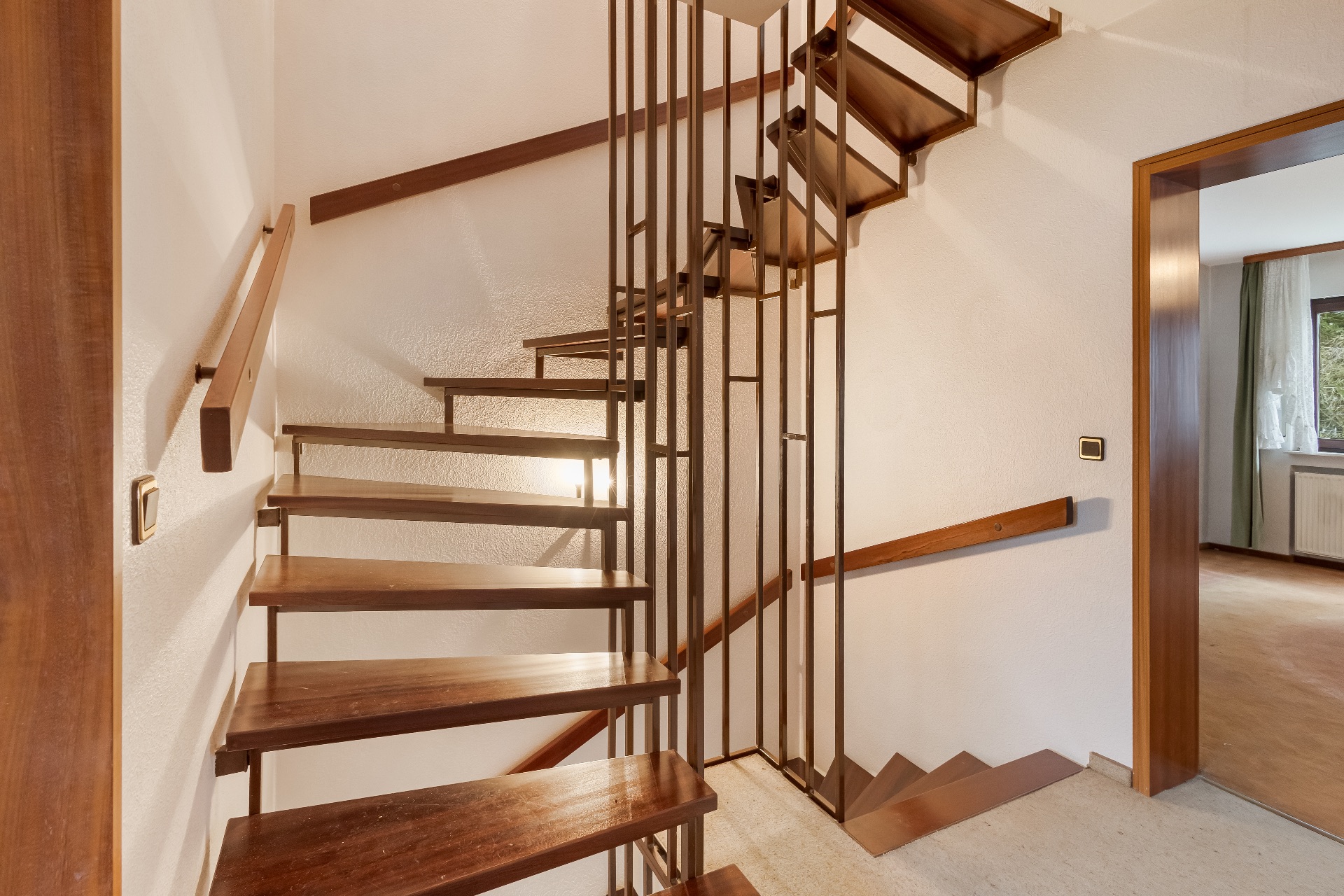 Offene Holztreppe mit Metallgeländer in einem Wohnhaus, daneben ein Raum mit Fenster.
