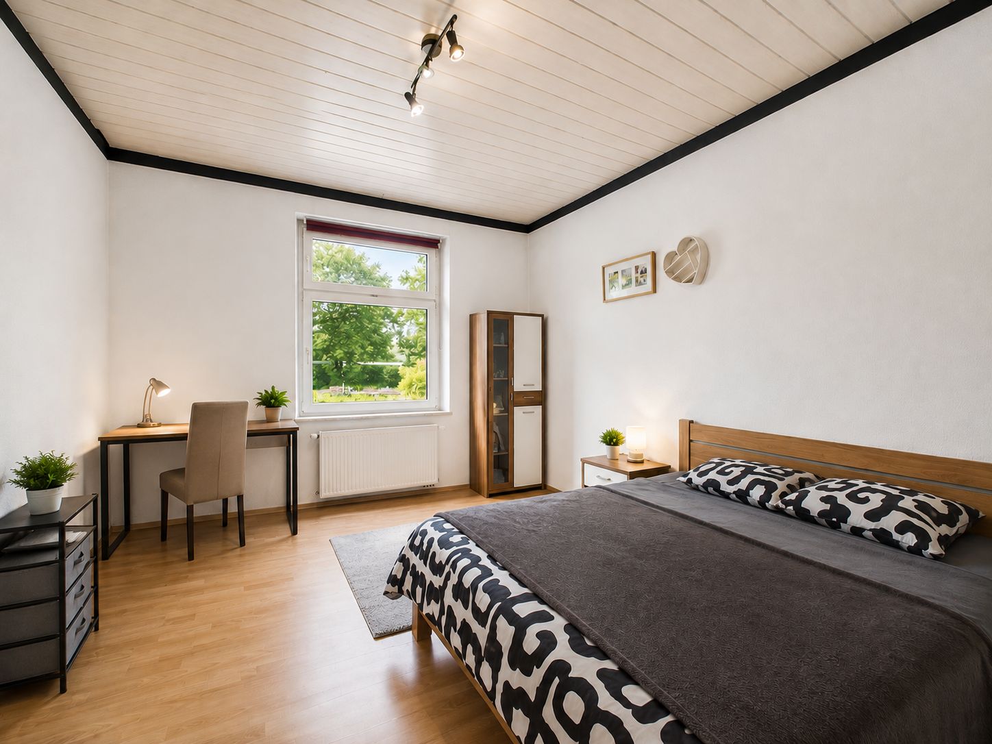 Helles Schlafzimmer mit Doppelbett, Schreibtisch, Fenster und Holzboden.