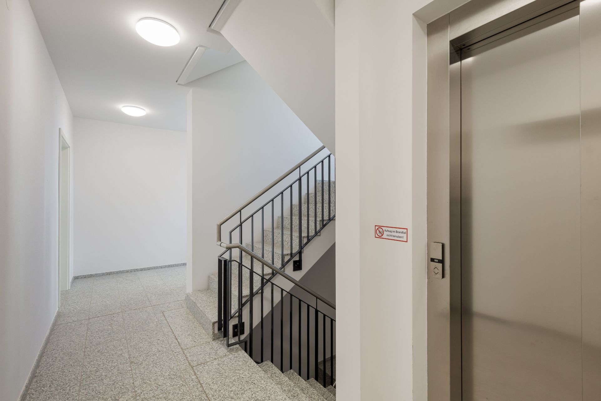 Heller Flur mit Treppenhaus und Aufzug in einem Wohngebäude.
