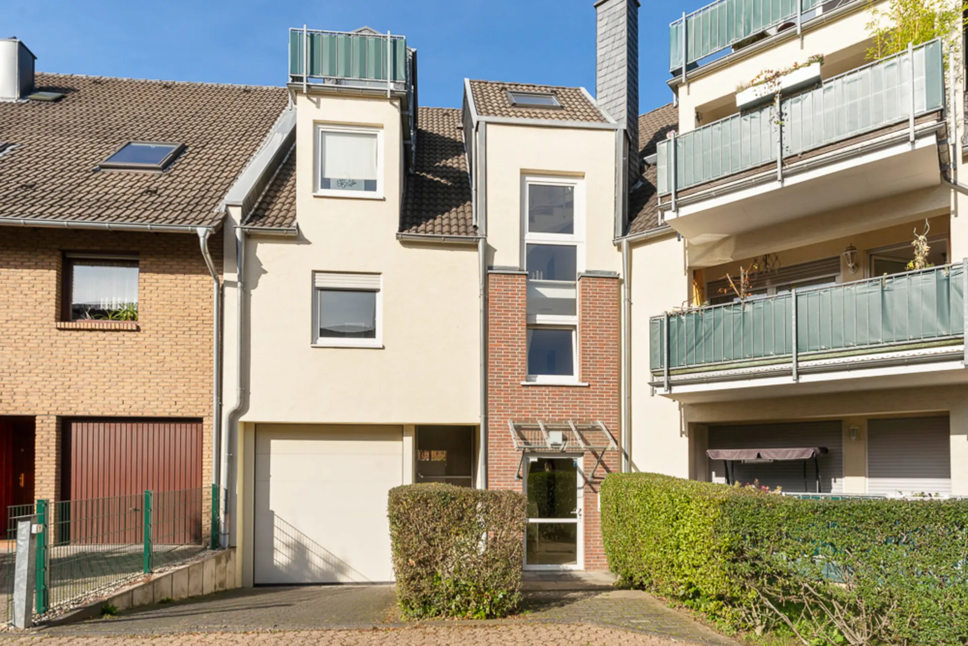 Moderne Fassade eines Reihenhauses mit Garage, großen Fenstern und gepflegtem Eingangsbereich.