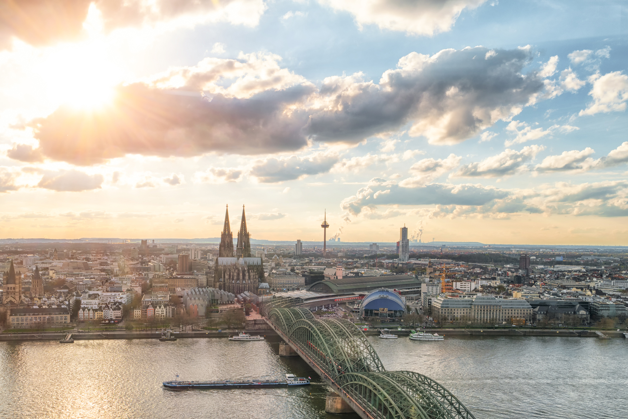 Stadtansicht mit Fluss, Brücke, Kathedrale und modernen Gebäuden bei Sonnenuntergang.