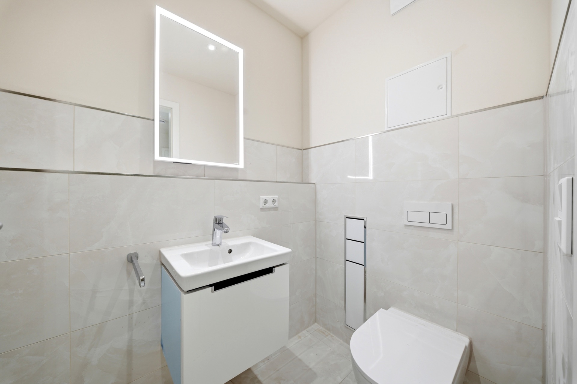 Modernes Badezimmer mit WC, Waschbecken, Spiegel und hellen Fliesen.