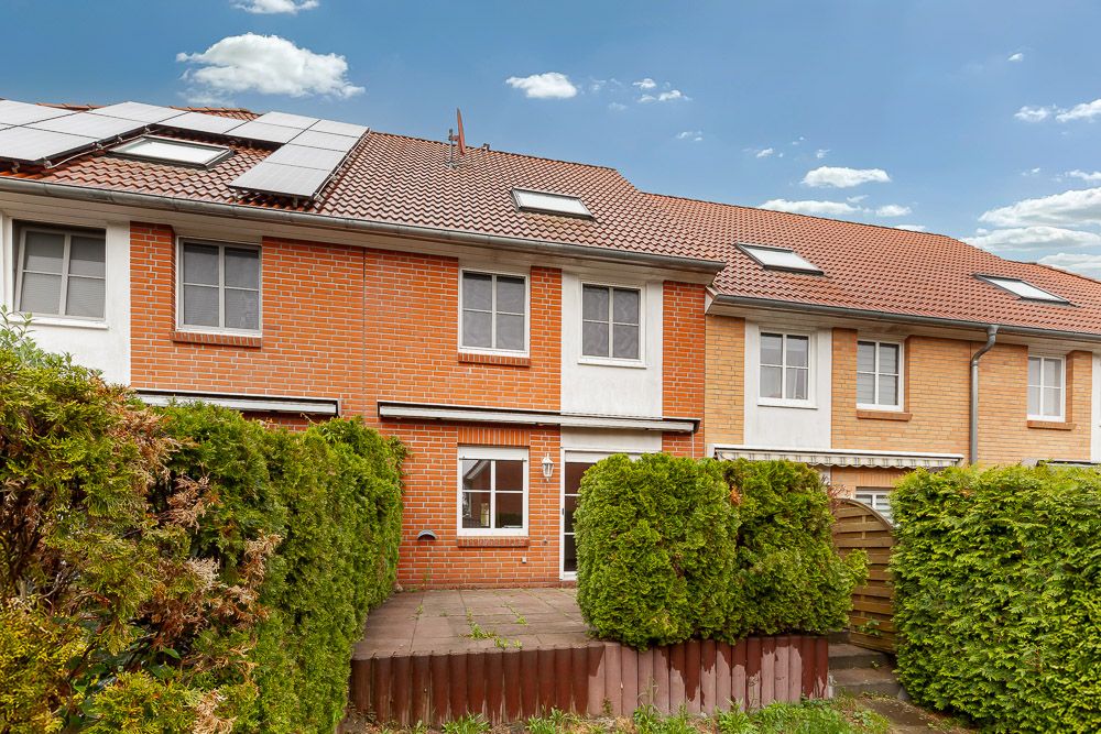 Rückseite eines Reihenhauses mit Terrasse, Ziegelwänden und umliegenden Hecken.