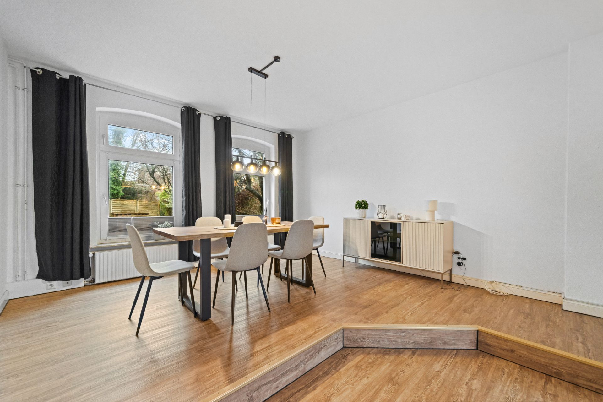 Essbereich mit Tisch, sechs Stühlen, Sideboard und großen Fenstern mit Vorhängen.