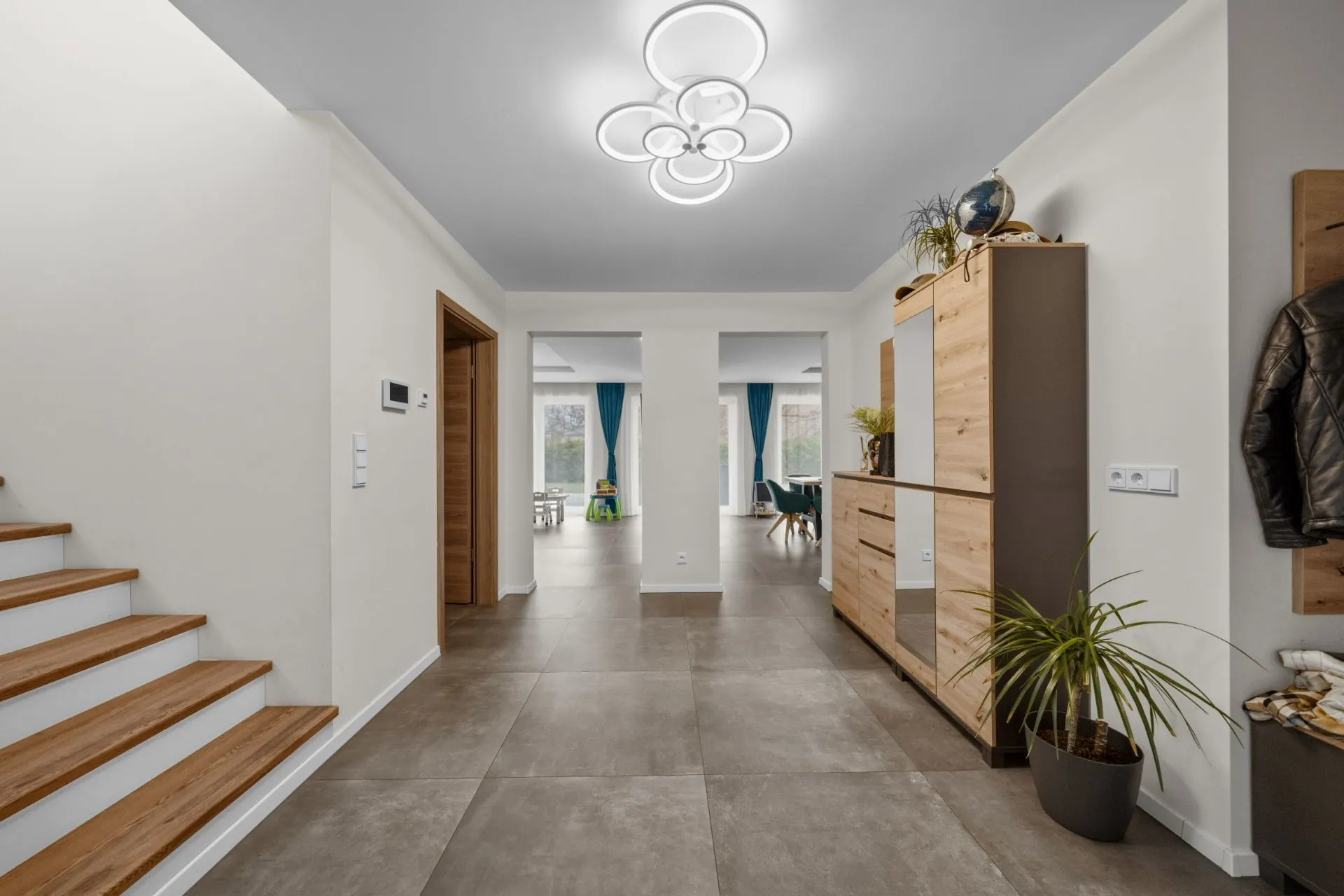 Heller Flur mit Treppe, Schrank, Pflanzen und modernem Deckenlicht in einem Wohnhaus.