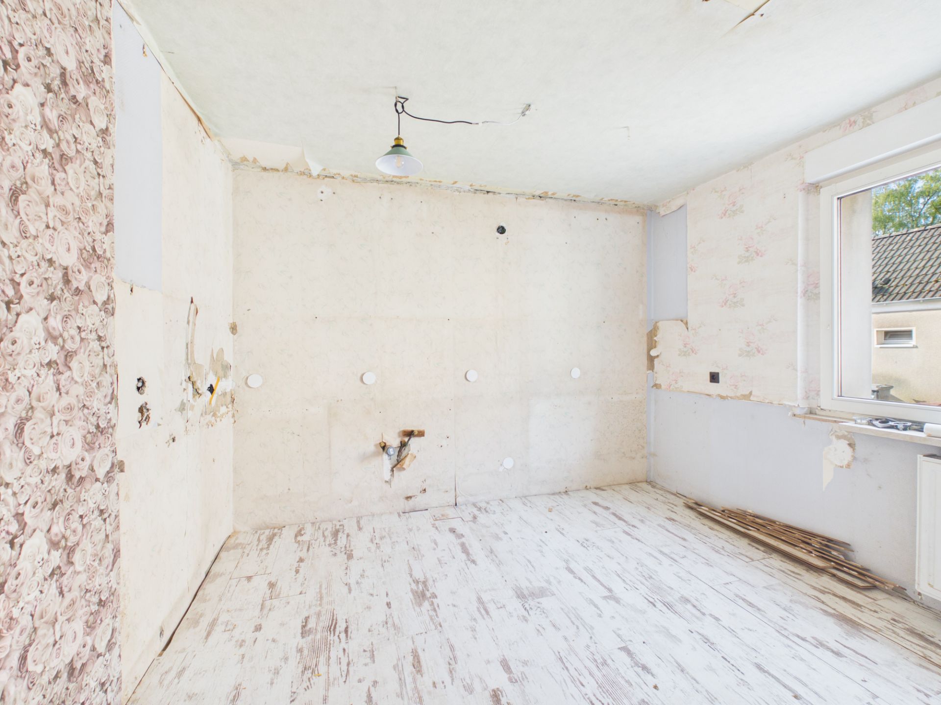 Leerer, renovierungsbedürftiger Raum mit alten Tapeten und offenem Fenster.