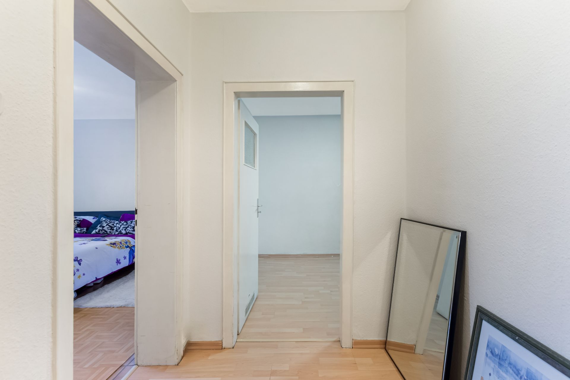 Heller Flur mit Laminatboden, zwei Türen, großem Spiegel und gerahmtem Bild an der Wand.
