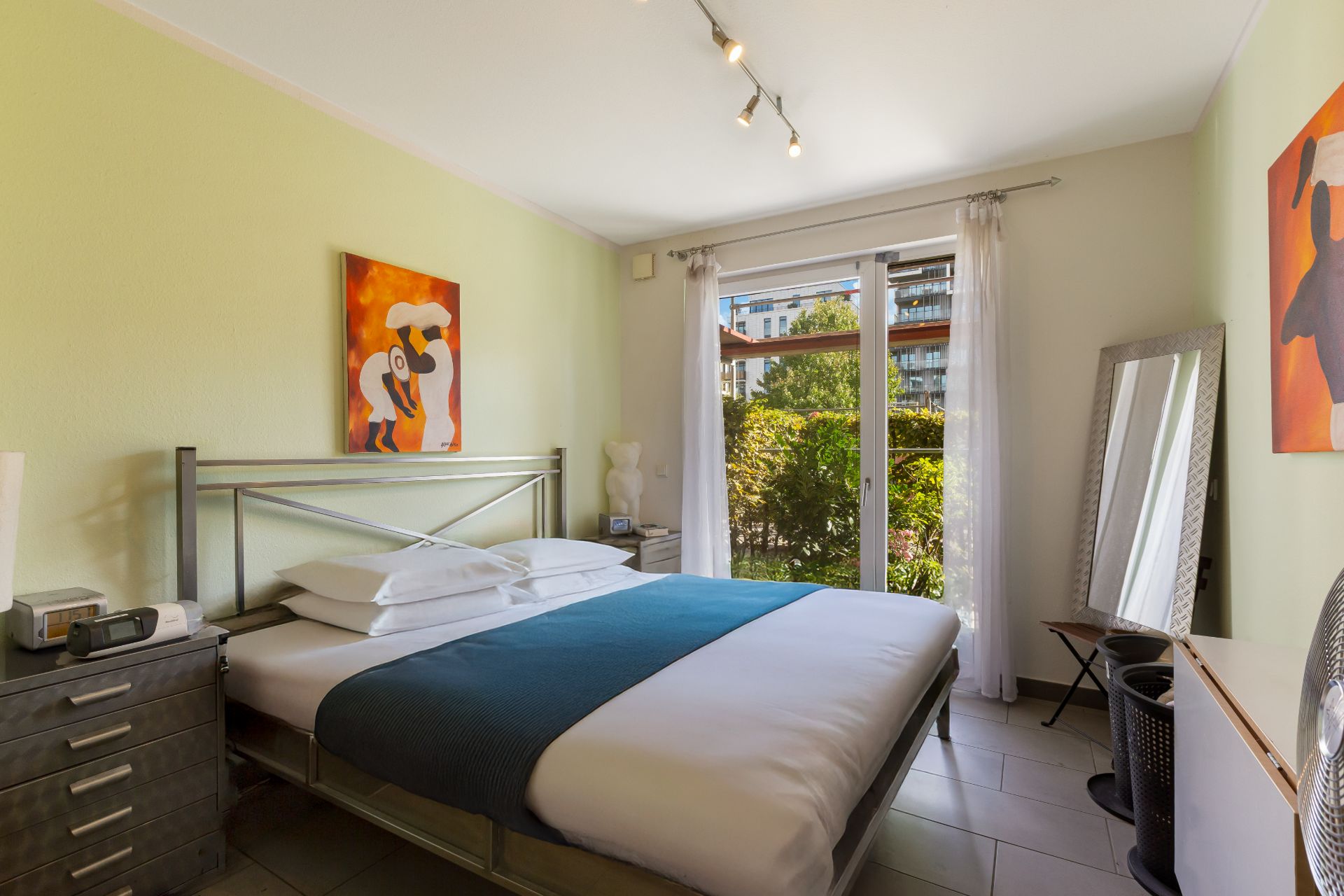 Helles Schlafzimmer mit Doppelbett, großem Fenster, Vorhängen und moderner Kunst an den Wänden.