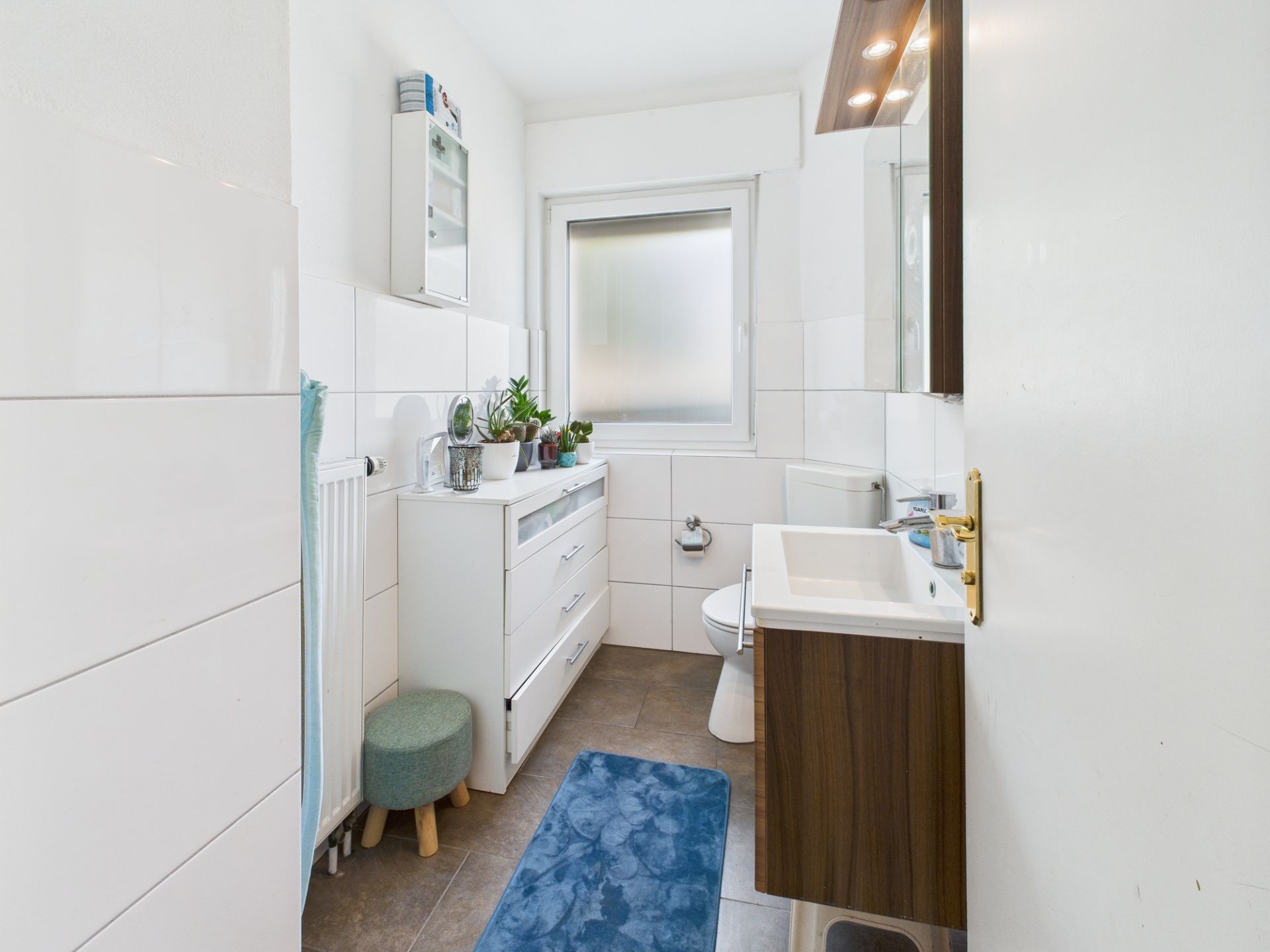 Helles Badezimmer mit Waschbecken, Toilette, Schrank, Pflanzen und fenster.