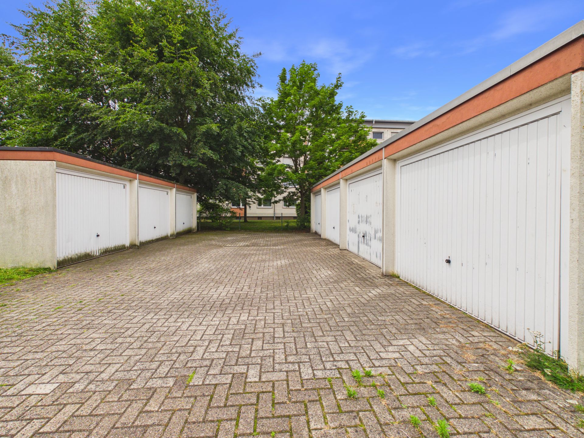 Gepflasterter Hof mit Garagen und Bäumen im Hintergrund.