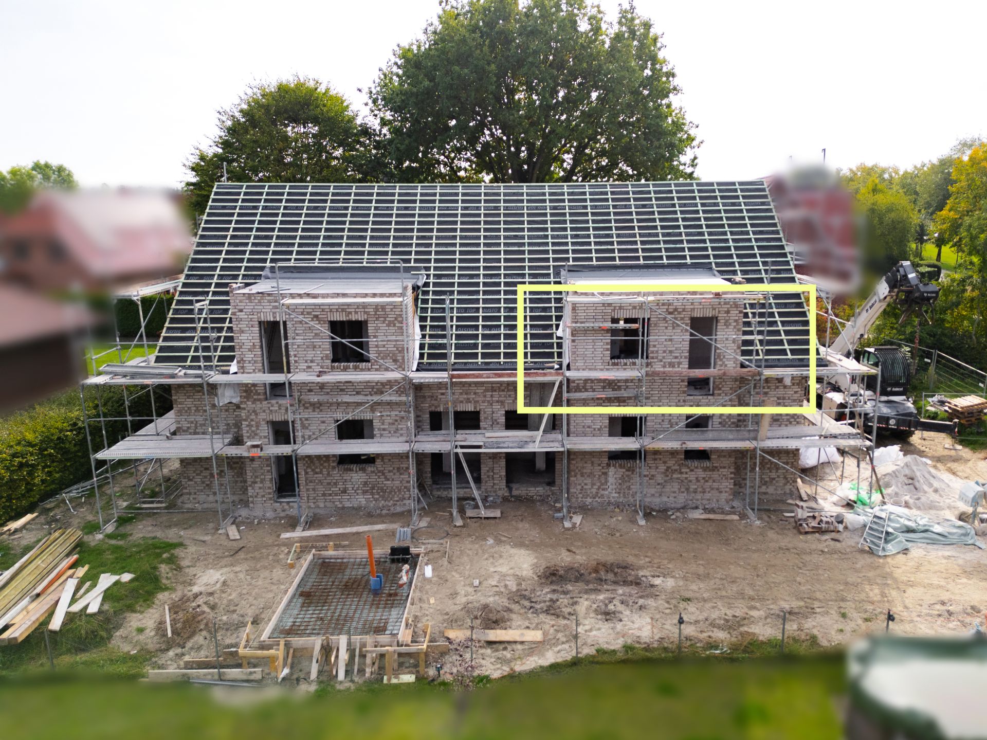 Backsteinhaus im Bau mit Gerüst und unfertigem Dach, Baustelle im Vordergrund.