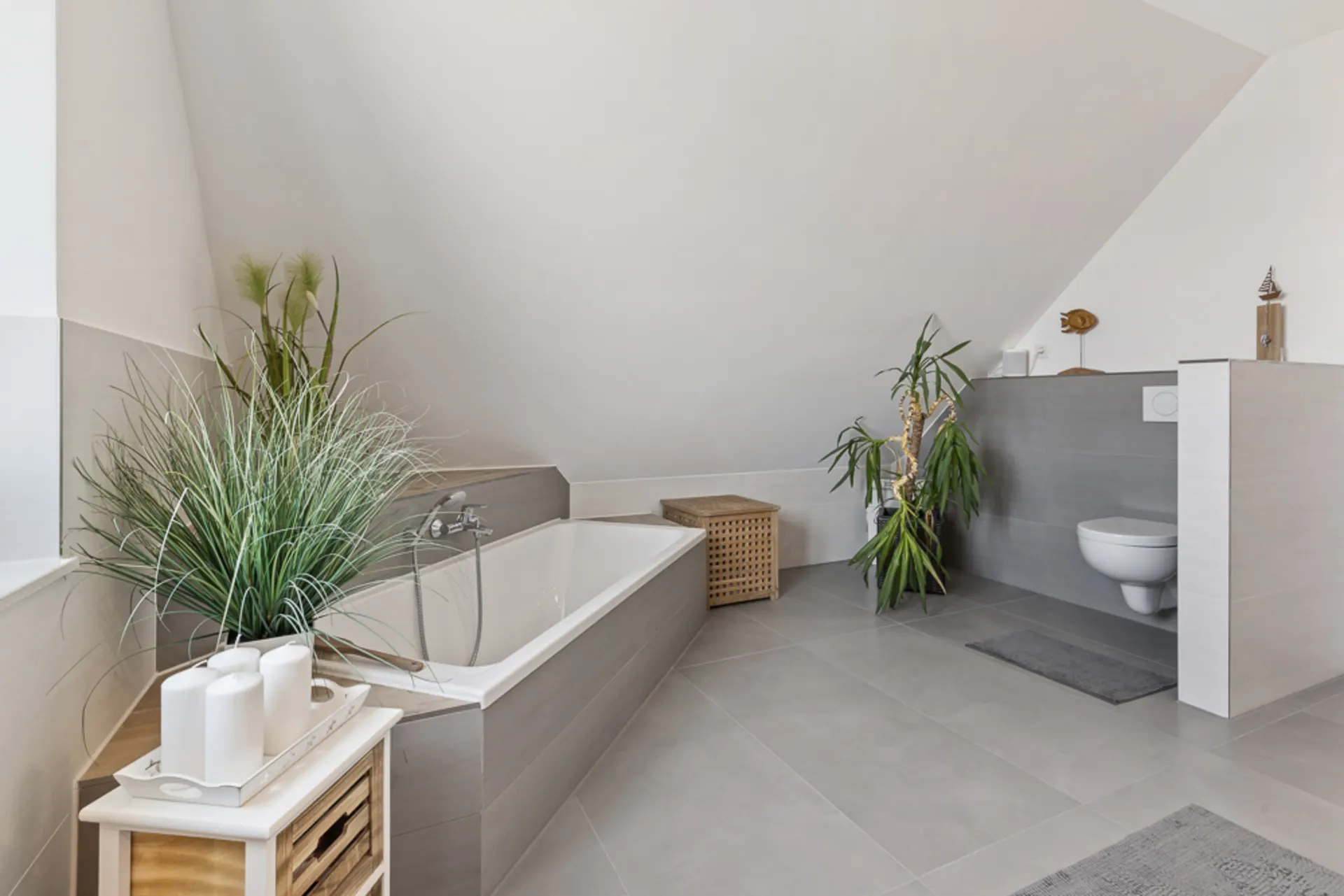Modernes Badezimmer mit Badewanne, Pflanzen, Wandtoilette und gefliestem Boden.