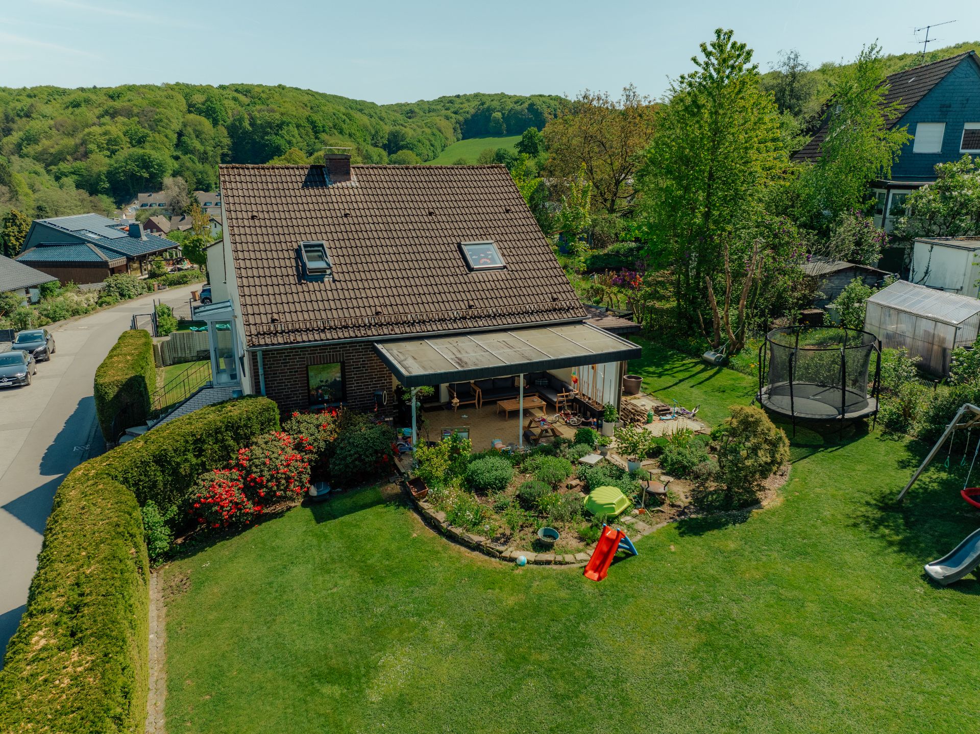 Haus mit Garten, Rutsche, Trampolin und überdachter Terrasse an einer ruhigen Straße.