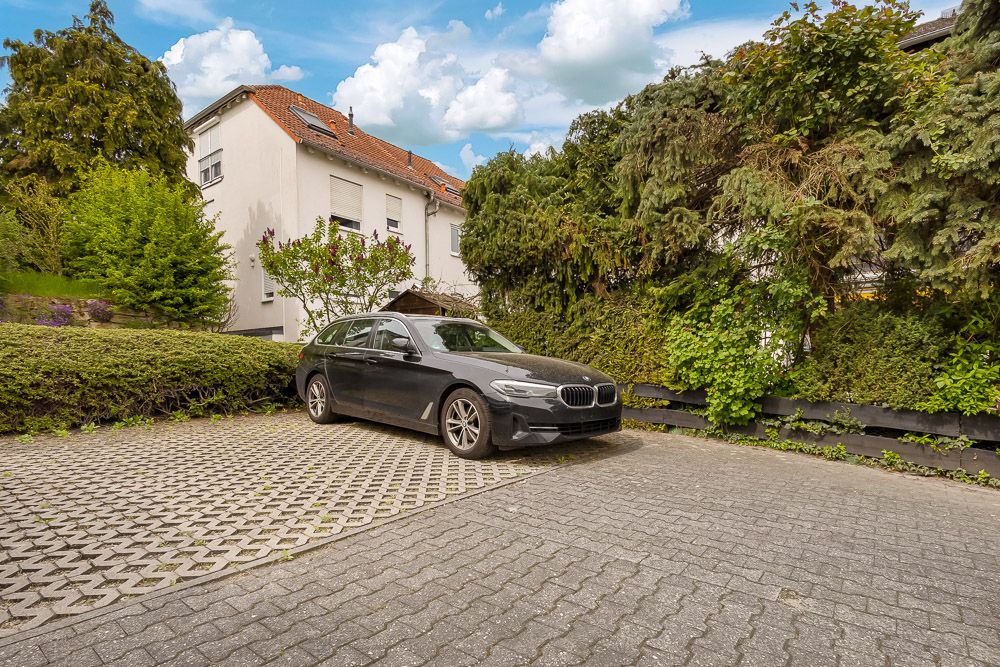 Schwarzer Kombi steht auf einem Parkplatz vor einem Wohnhaus mit viel Grün.