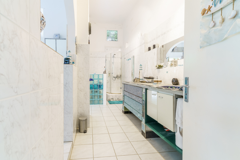 Helles Badezimmer mit großer Dusche, langem Waschbecken und weißen Fliesen.