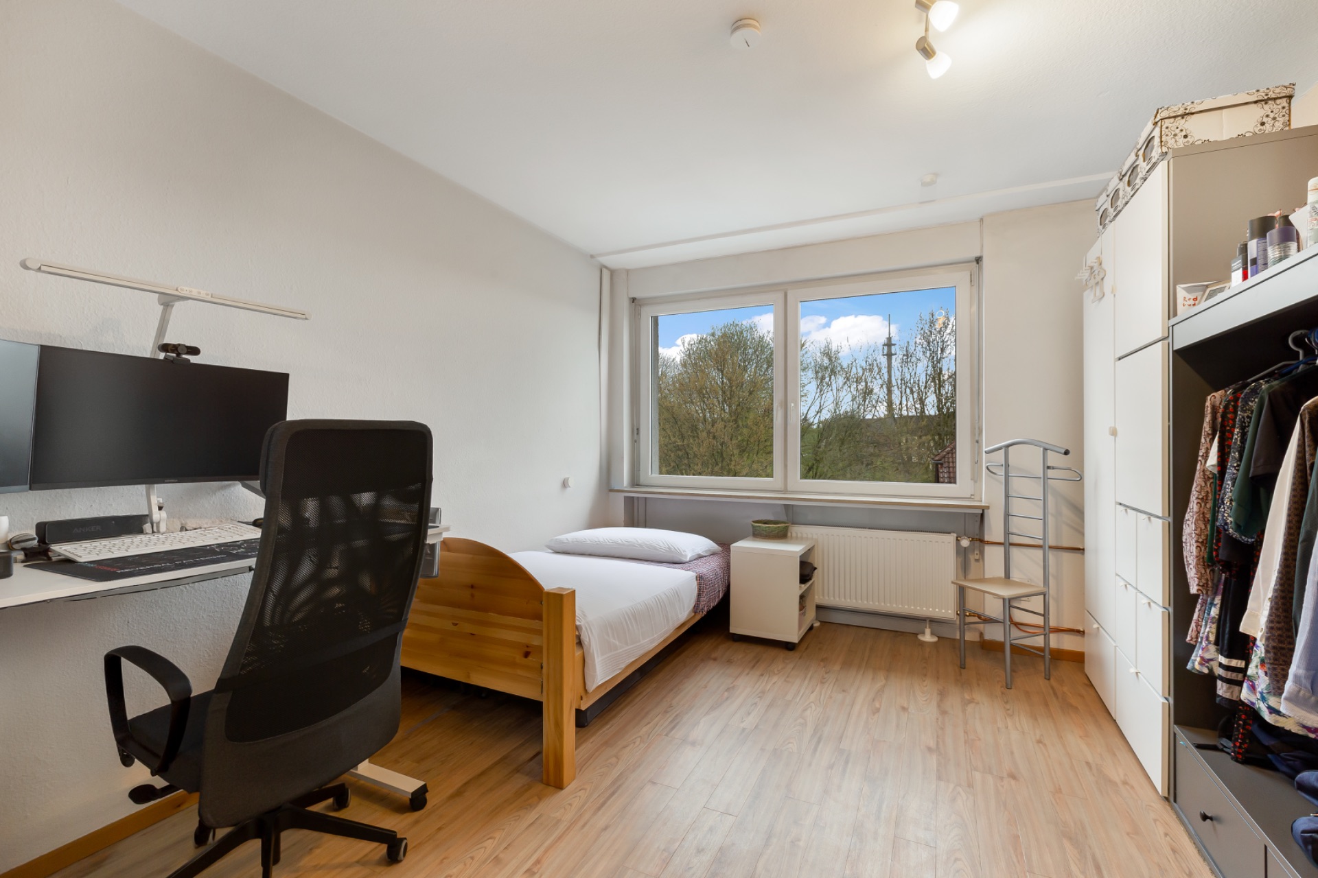 Helles Schlafzimmer mit Einzelbett, Schreibtisch, Stuhl, großem Fenster und Kleiderschrank.