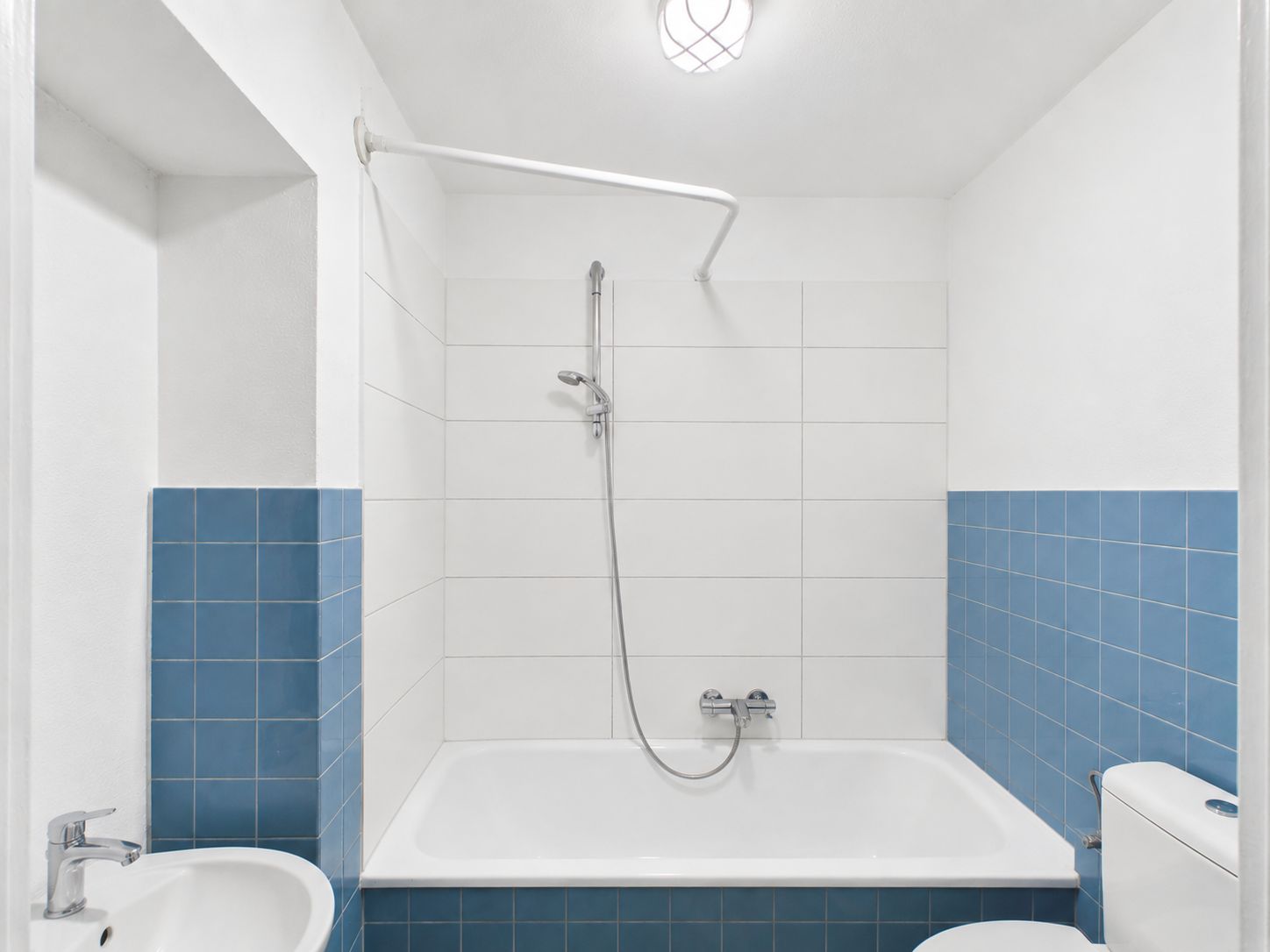 Badezimmer mit Badewanne, Dusche, blau-weißen Fliesen und WC.