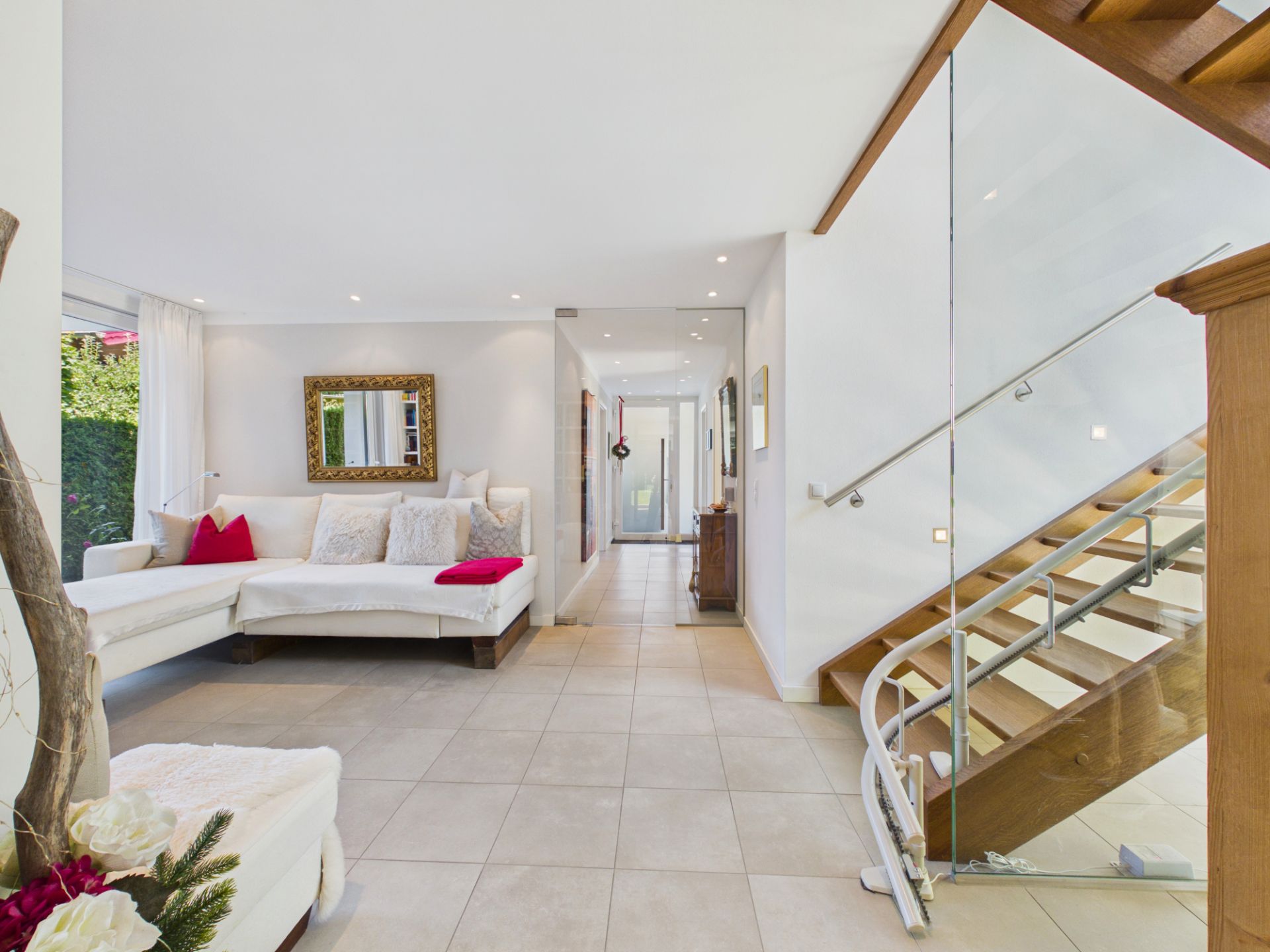 Helles Wohnzimmer mit weißem Sofa, Spiegel an der Wand und moderner Holztreppe mit Glasgeländer.