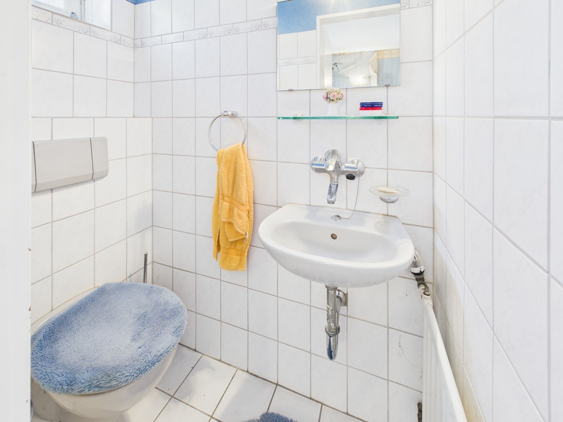 Kleines Badezimmer mit WC, Waschbecken, Spiegel und gelbem Handtuch.