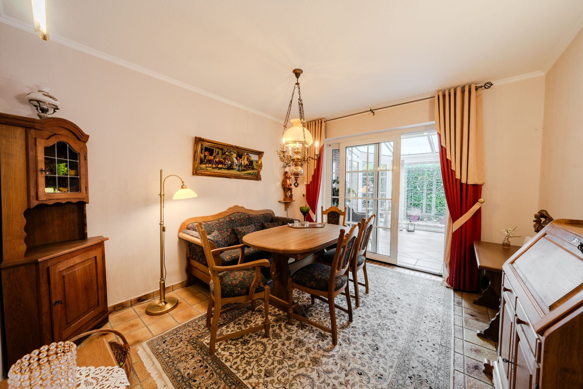 Gemütliches Esszimmer mit Holzmöbeln, Teppich und großem Fenster mit Blick auf Terrasse.
