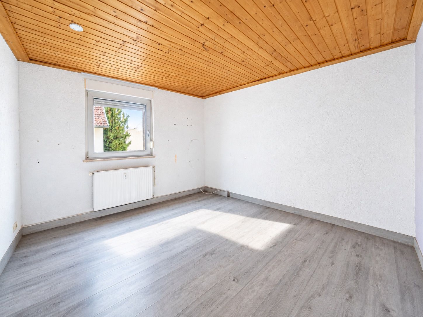 Leerer Raum mit Holzdecke, grauem Boden und Fenster an der Wand.