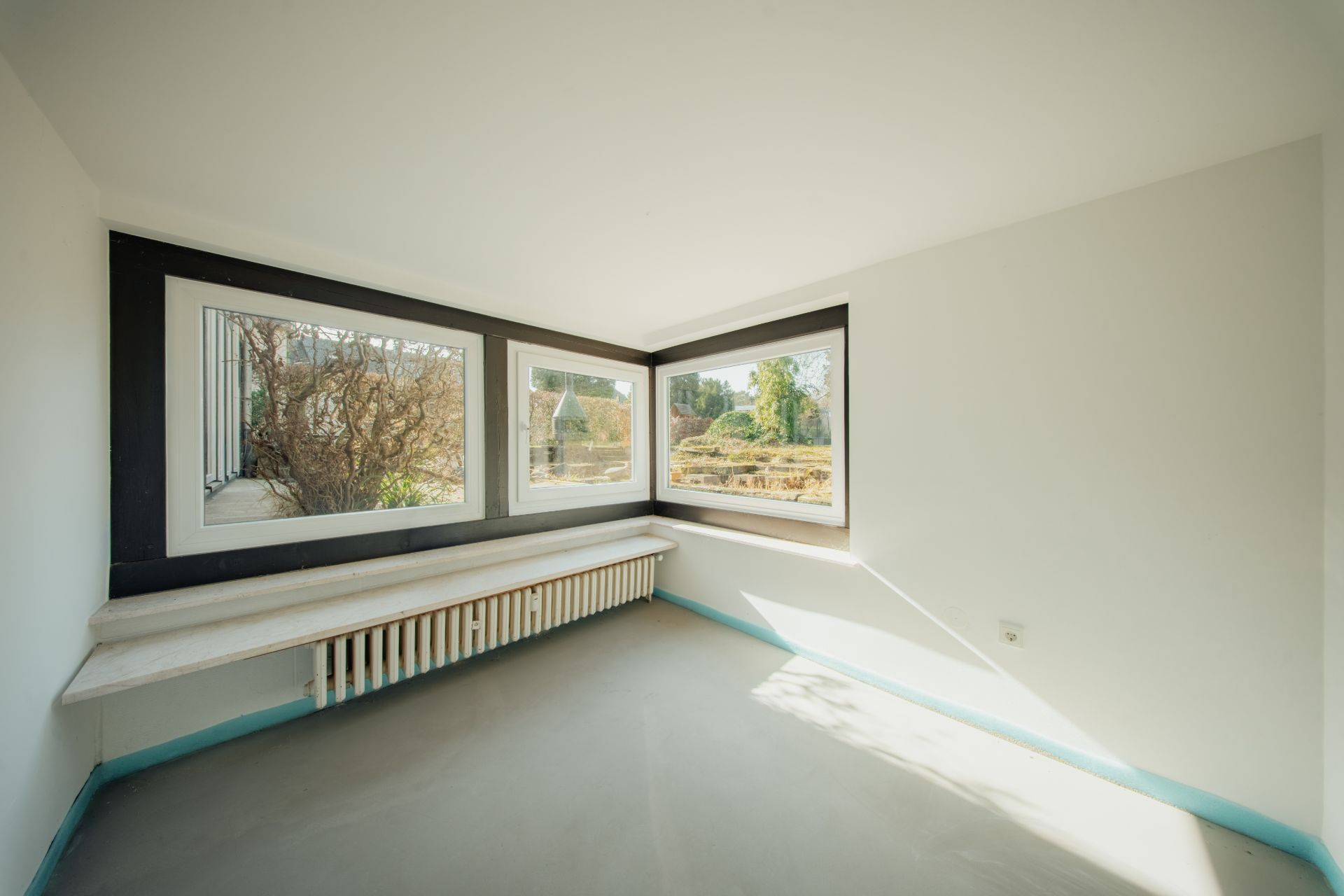 Heller Raum mit zwei großen Eckfenstern und einer langen Fensterbank.