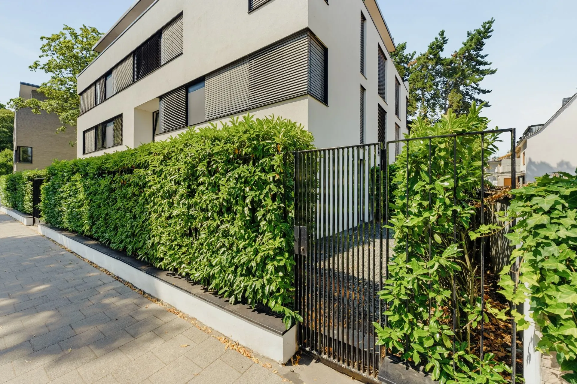 Modernes Wohngebäude mit schwarzem Zaun und dichter grüner Hecke entlang des Gehwegs.