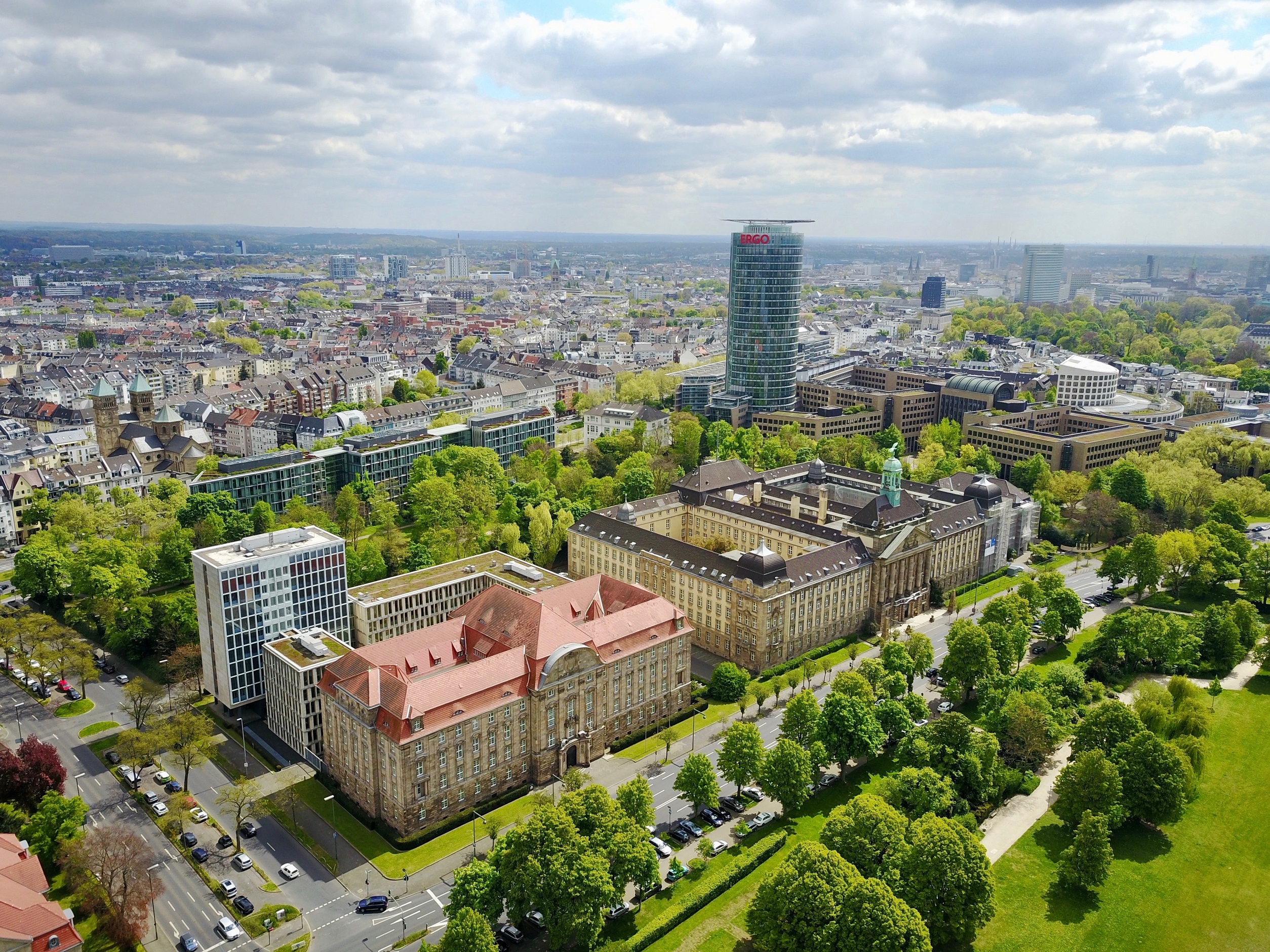 Luftaufnahme einer Stadt mit großen Gebäuden, vielen Bäumen und Straßen im Vordergrund.