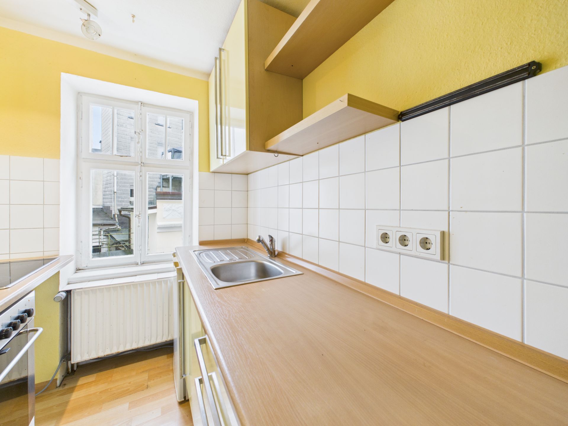 Helle Küche mit gelber Wand, Spüle, Herd, großem Fenster und weißen Fliesen an der Wand.