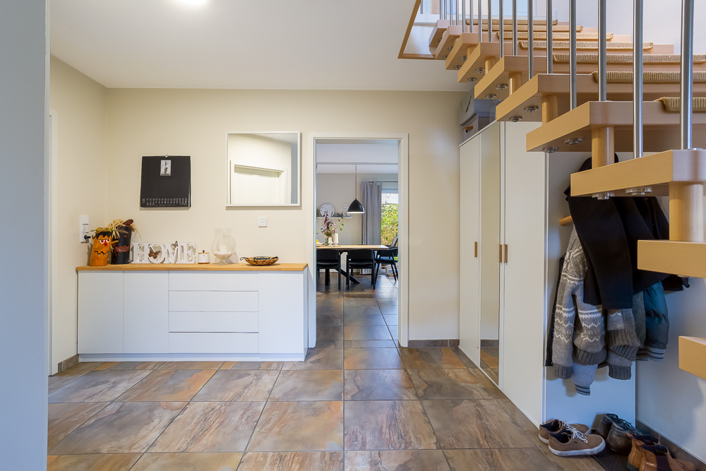 Heller Flur mit Garderobe, Kommode, Spiegel und Treppe, im Hintergrund ein Esszimmer.