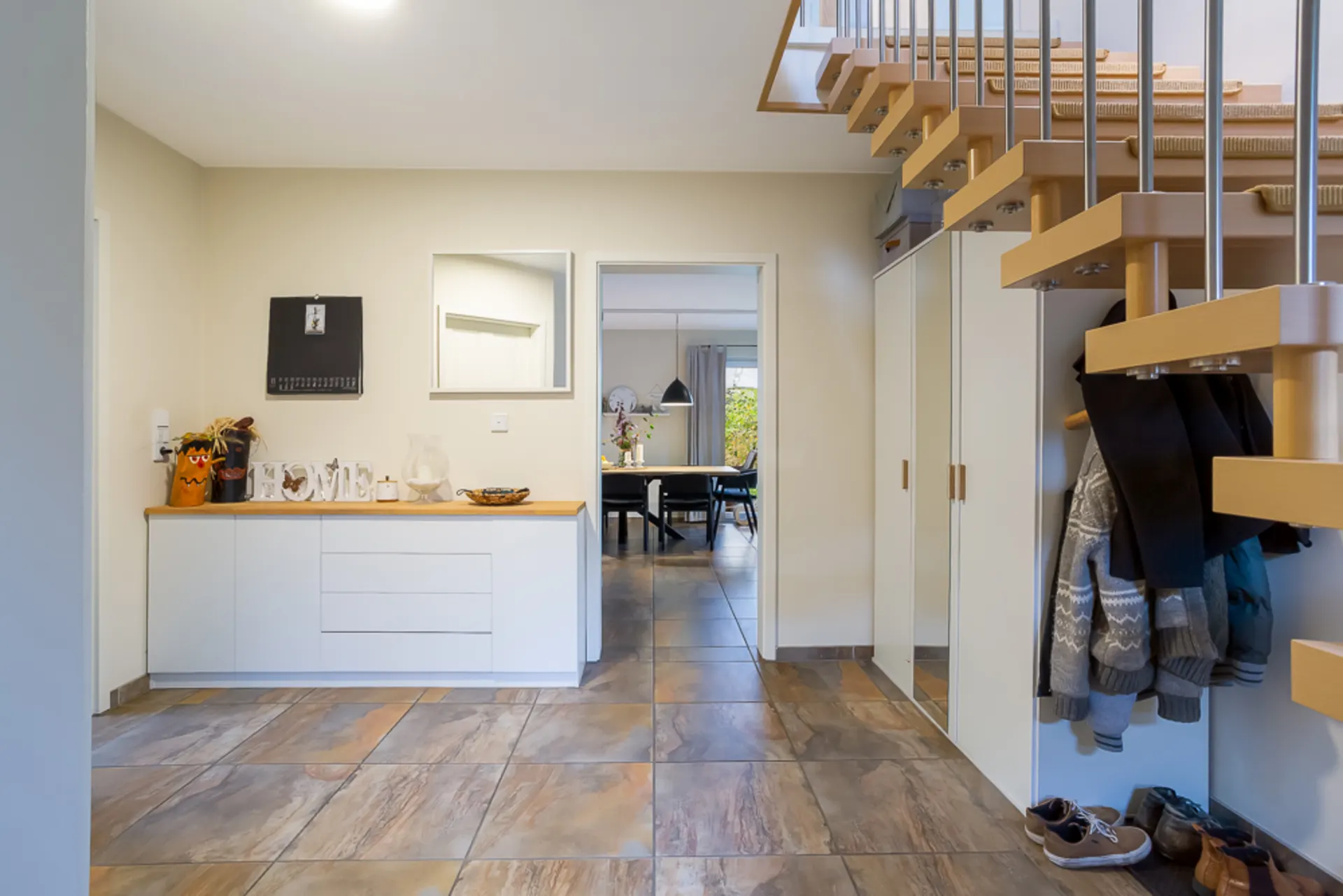 Heller Flur mit Garderobe, Kommode, Spiegel und Treppe, im Hintergrund ein Esszimmer.