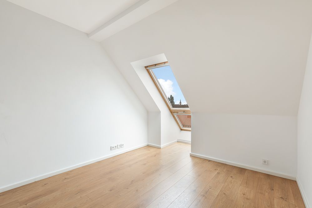 Leerer Raum mit Dachschrägen, Holzfußboden und großem Dachfenster.