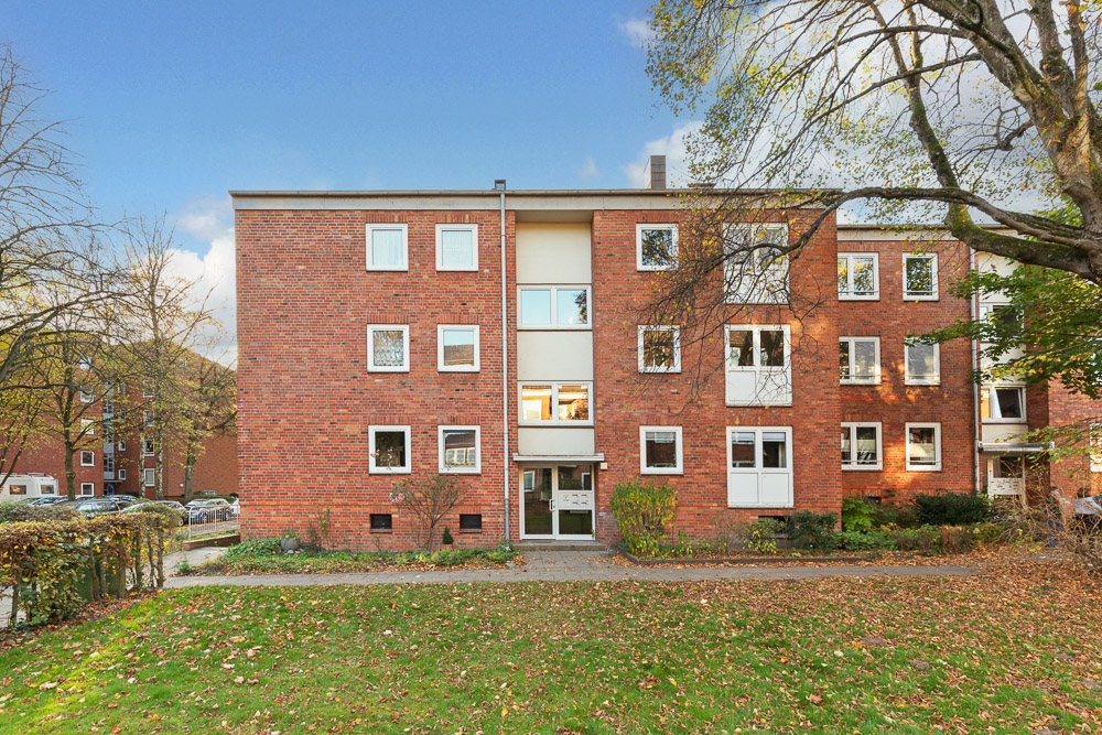Dreistöckiges Wohnhaus aus rotem Backstein mit mehreren Fenstern und einem Eingangsbereich.