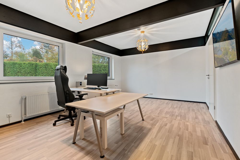 Helles Arbeitszimmer mit zwei Schreibtischen, Computer, Stuhl und großen Fenstern.