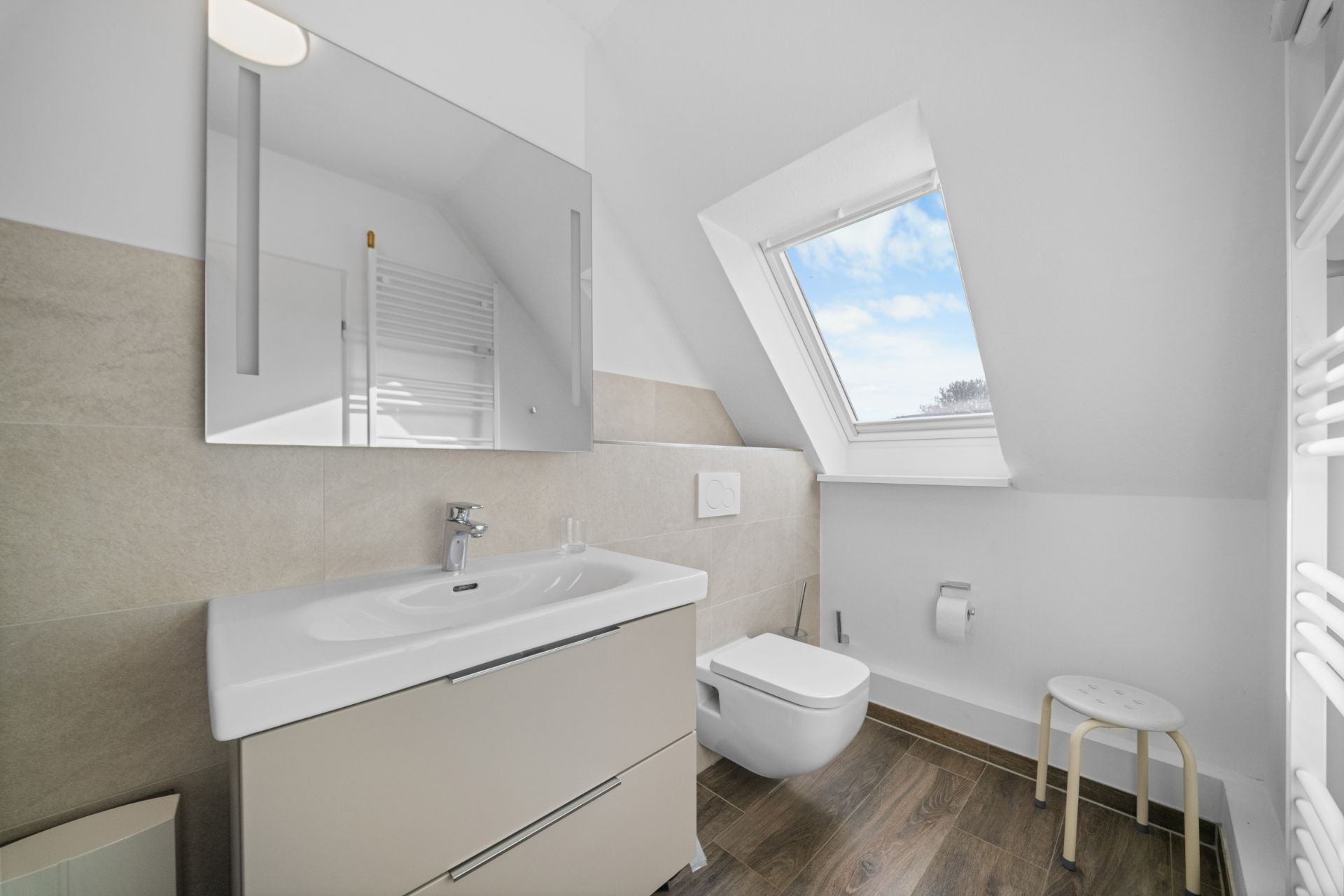 Modernes Badezimmer mit Waschbecken, Spiegel, Toilette und großem Dachfenster.