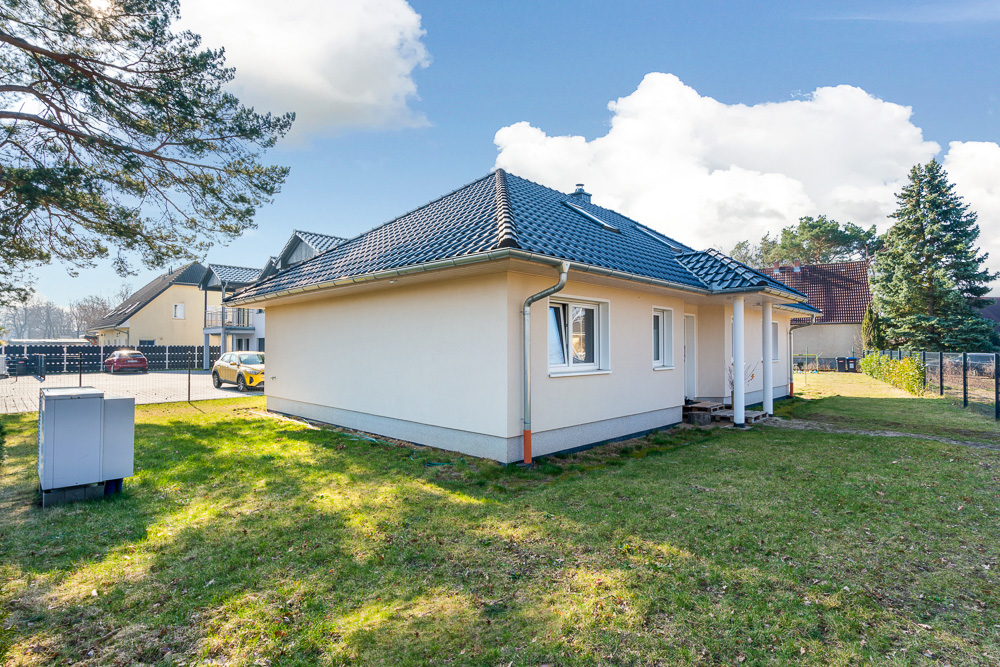 Einfamilienhaus mit hellem Putz, dunklem Dach und kleinem Garten bei sonnigem Wetter.